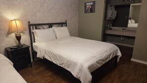 A bedroom with a bed, a nightstand with a lamp, a dresser, and a mirror. - Burnham's Lodging (San Saba)