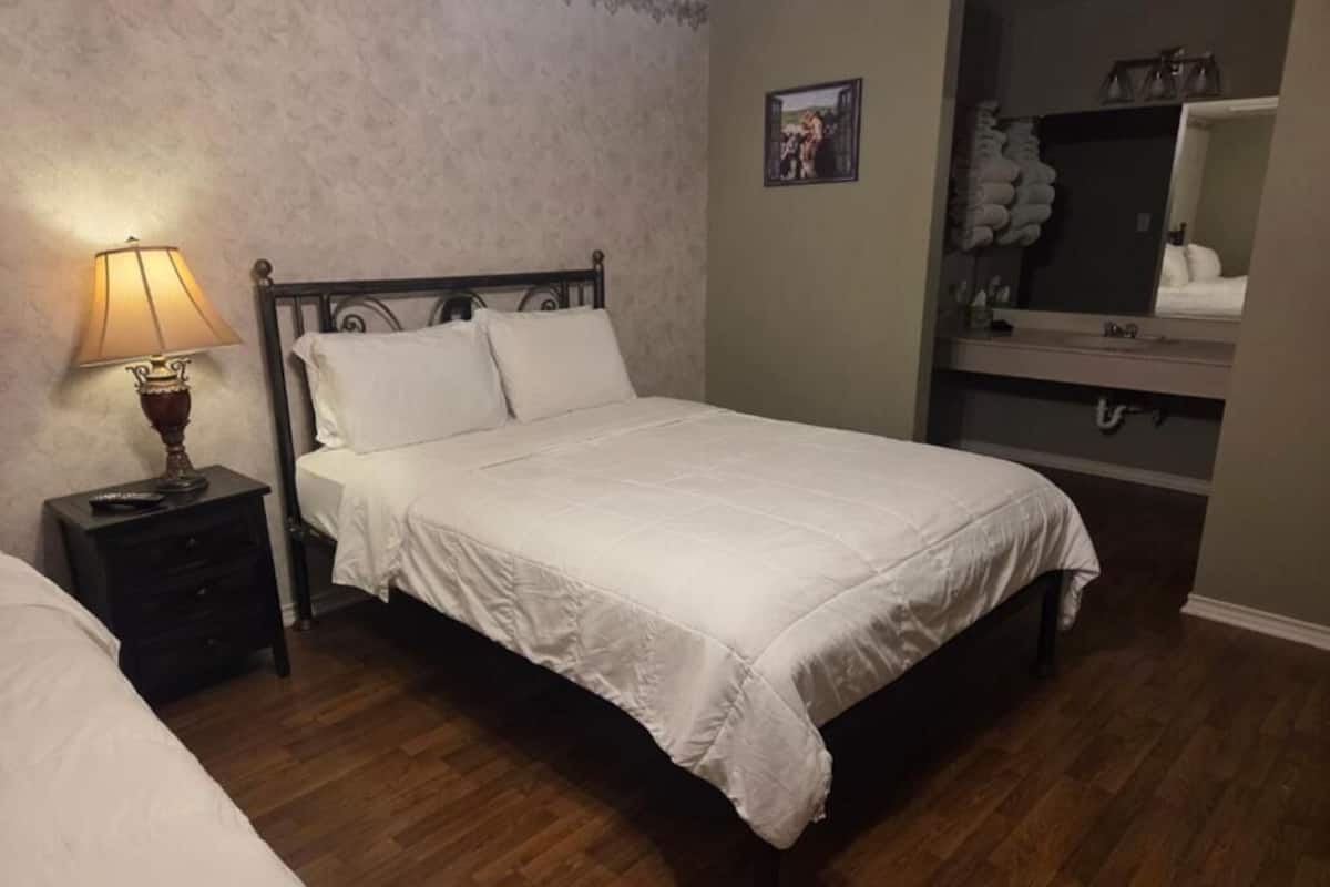 A bedroom with a bed, a nightstand with a lamp, a dresser, and a mirror.