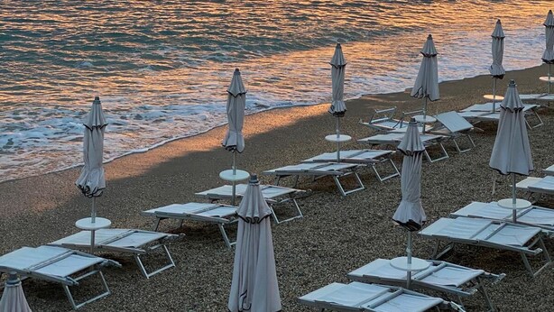 A beach with sun loungers and umbrellas, a calm sea, and a sunset with mountains in the background. - Cozy accommodation a short walk from the sea and downtown with private parking space (Finale Ligure)