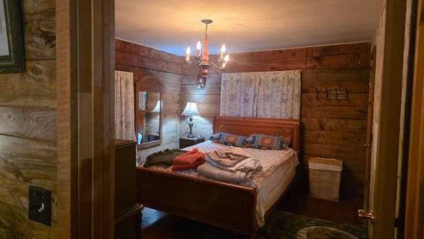 Ein Schlafzimmer mit Holzwänden, einem Bett, einem Nachttisch, einer Lampe, einem Spiegel und einer Chandelieber.