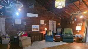 Ein rustikales Interieur mit Holzwänden, einer großen Holzbalkendecke und einer Mischung an Sitzgelegenheiten, darunter eine Couch, Sessel und ein Sessel mit Decke.