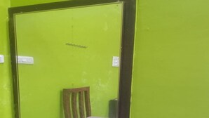 A narrow hallway with green walls, a wooden chair, and a door with a sign above it.