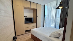 Una camera da letto moderna con pavimento in legno, un letto con biancheria bianca, una TV su un mobile in legno e una lampada a sospensione.