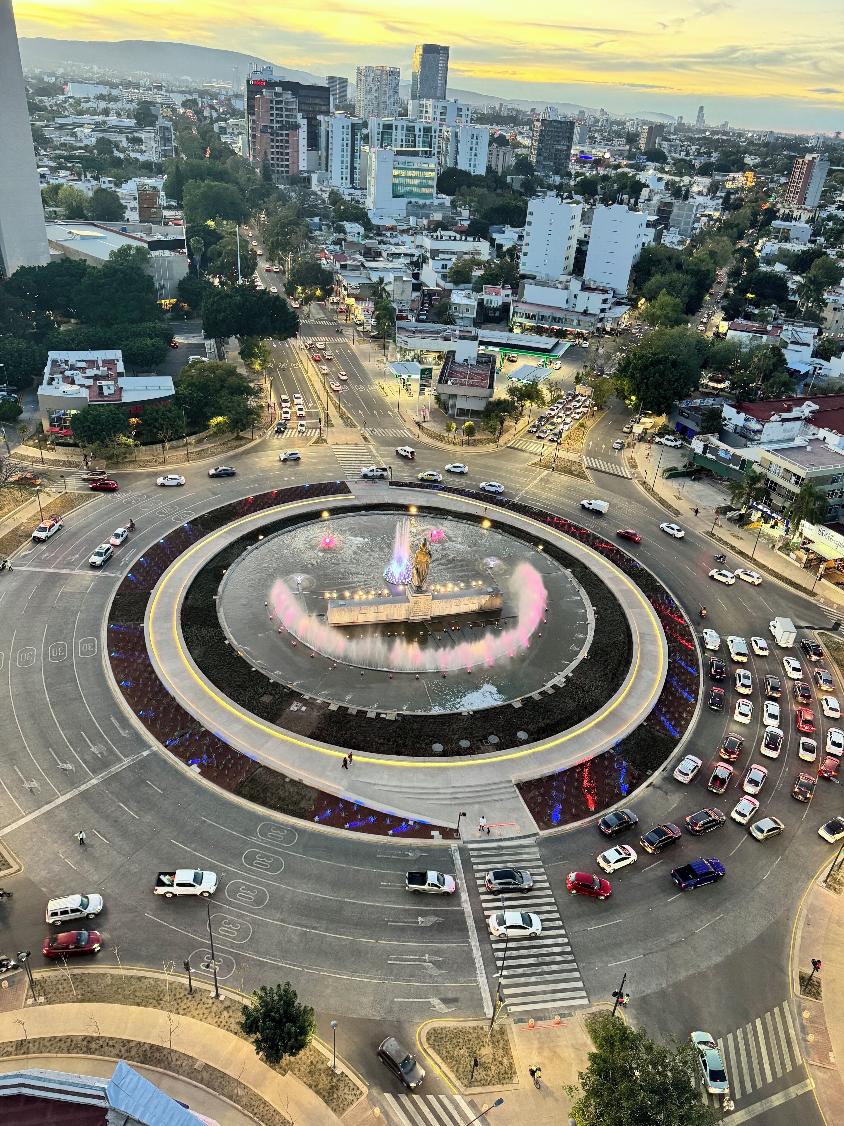 A roundabout with a central fountain, surrounded by roads and buildings.