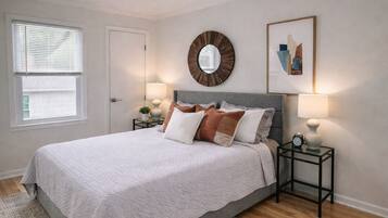 Une chambre à coucher avec un lit, des tables de chevet, un miroir et un tableau encadré au mur.