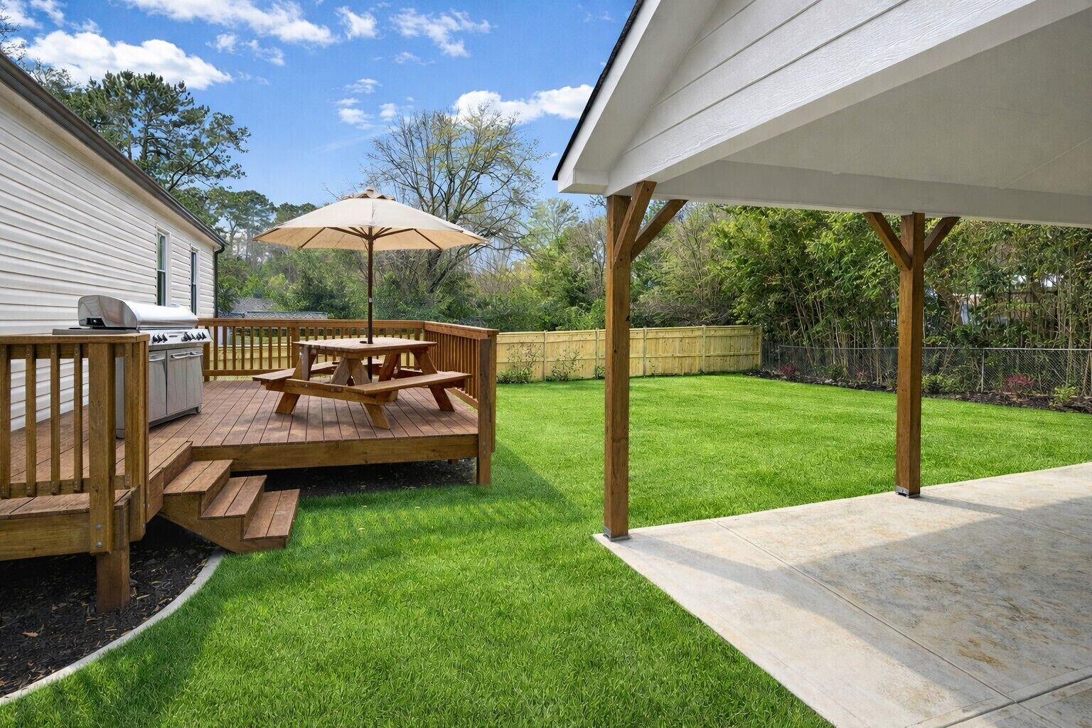 Un jardin avec une terrasse en bois, une table de pique-nique et un barbecue.