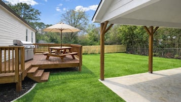 Un jardin avec une terrasse en bois, une table de pique-nique et un barbecue.