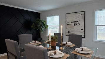 Un espace repas avec une table en verre, des chaises recouvertes d’un tissu gris et un mur d’accent noir.