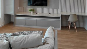 A modern living room with a sofa, a flat-screen TV mounted on the wall, a dining area with a table and chairs, and a wooden floor. - Tropical Executive Suíte Flat 1001 | Ponta Negra | (Manaus)