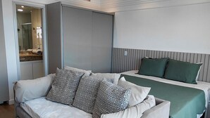 A modern bedroom with a large bed, a smaller sofa, and a separate sleeping area. - Tropical Executive Suíte Flat 1001 | Ponta Negra | (Manaus)