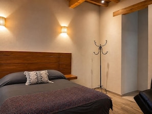 Een slaapkamer met een houten hoofdeinde, een bed met grijze beddengoed, een vloerlamp en een kapstok.