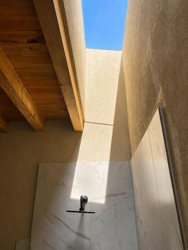 A room with a wooden ceiling, a white tiled floor, and a view of the sky.