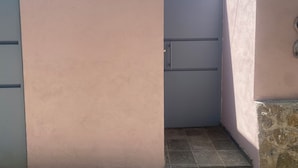 Ein schmaler Flur mit einer geschlossenen Tür, gefliestem Boden und einer Steinwand.