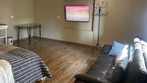 Ein Zimmer mit einer Couch, einem kleinen Tisch, einem an der Wand befestigten Fernseher und einem Kleiderhaken.
