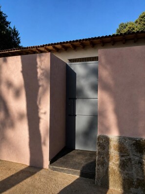 Une entrée d’immeuble avec un portail métallique fermé, un chemin en béton et un mur à la surface texturée.