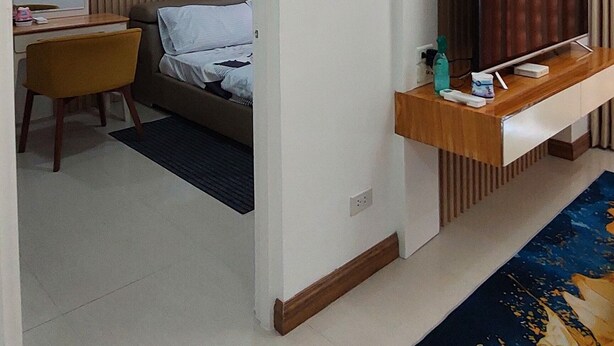 A hotel room with a bed, a desk with a chair, a TV on a wooden stand, and a ceiling-mounted air conditioner. - Unit 706-One Bedroom Unit at One Pontefino Tower (Batangas City)