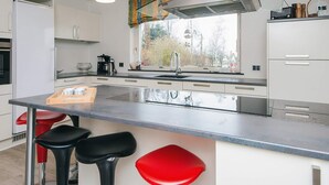 Una cocina moderna con armarios blancos, una isla grande con taburetes, una estufa a gas y una ventana con vista a árboles.
