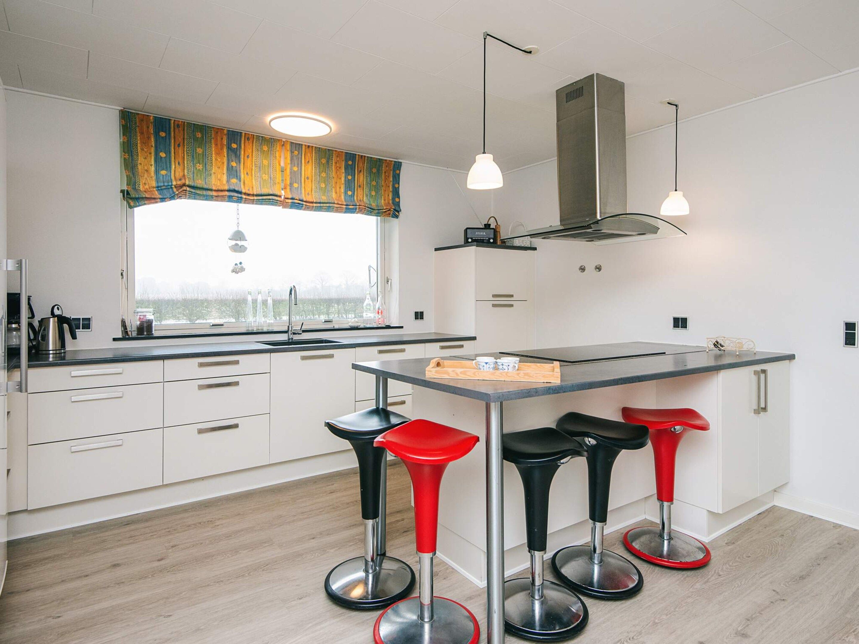 Een moderne keuken met witte kastjes, een centraal eiland met krukken, hanglampen en uitzicht door het raam.