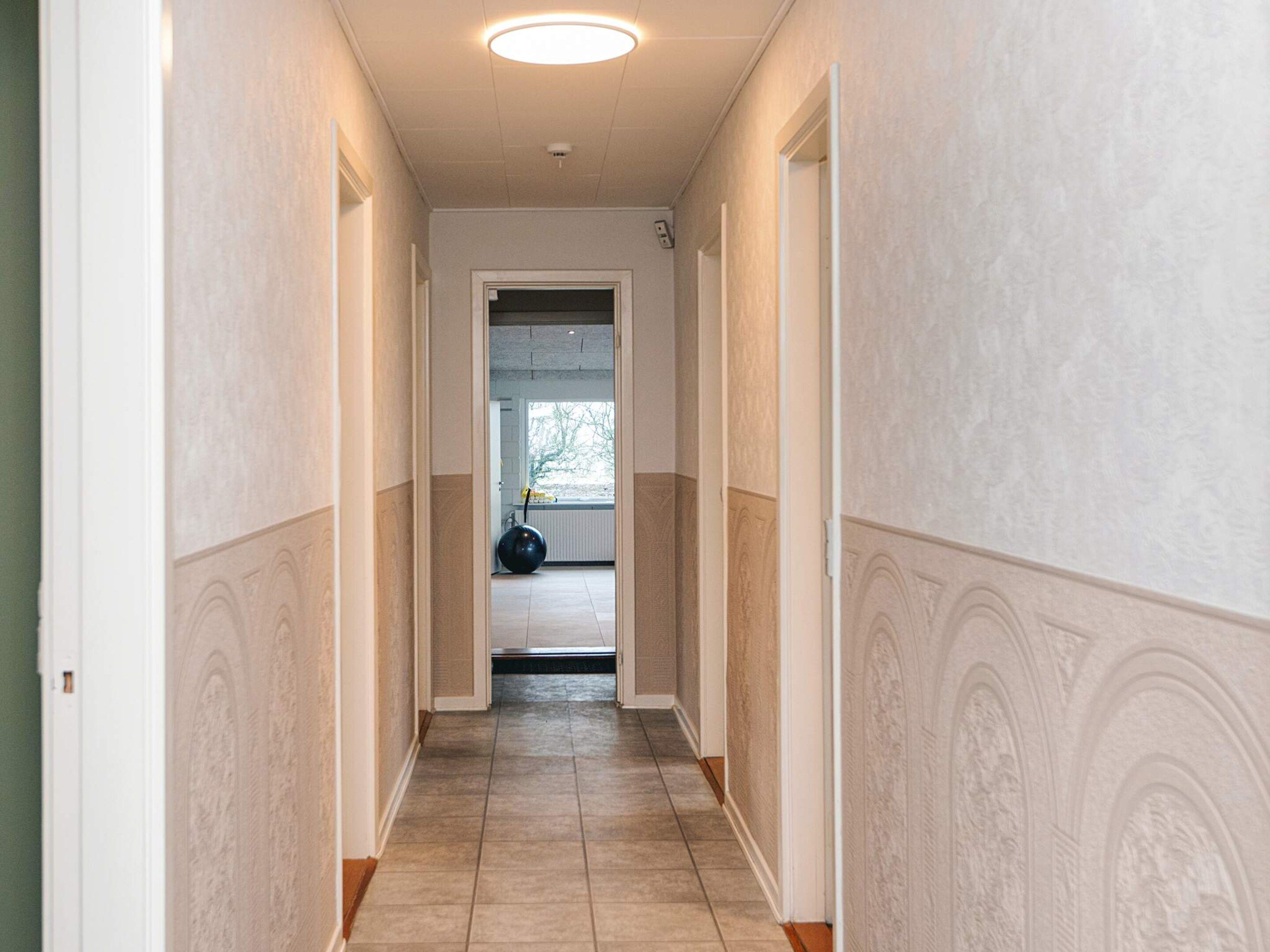 Un corridoio con un lampadario a soffitto, una porta in fondo e un termosifone sulla parete.