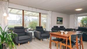 Una sala de estar moderna con una mesa de comedor de madera, sofás grises y un ventanal con vistas al exterior.