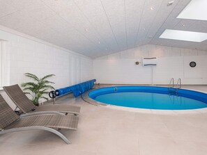 An indoor swimming pool with a blue water feature, surrounded by lounge chairs and a potted plant. - 4 Star Holiday Home in Allingabro (Allingåbro)