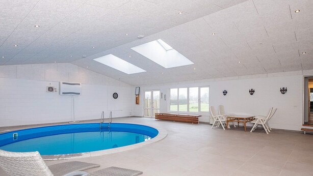 Una piscina interior con sillas de descanso, una mesa y vistas al exterior.