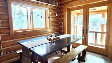 A wooden interior with a large dining table, benches, and a window with a view of trees.