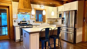Una cocina moderna con vigas de madera, armarios blancos, electrodomésticos de acero inoxidable y una isla central con taburetes de bar.
