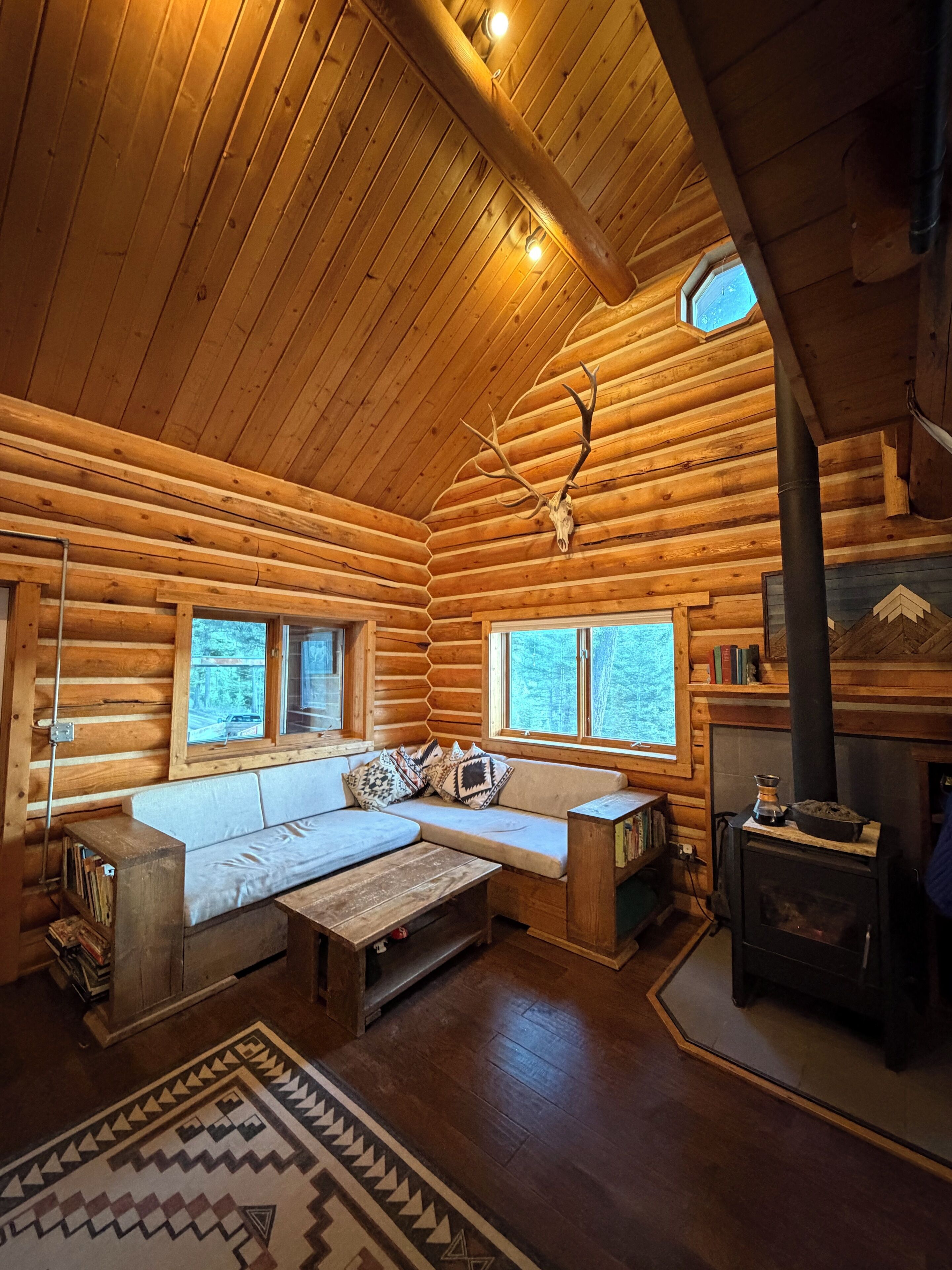Ein Holzblockhaus-Innenraum mit einer Couch, Kamin und Fenstern.