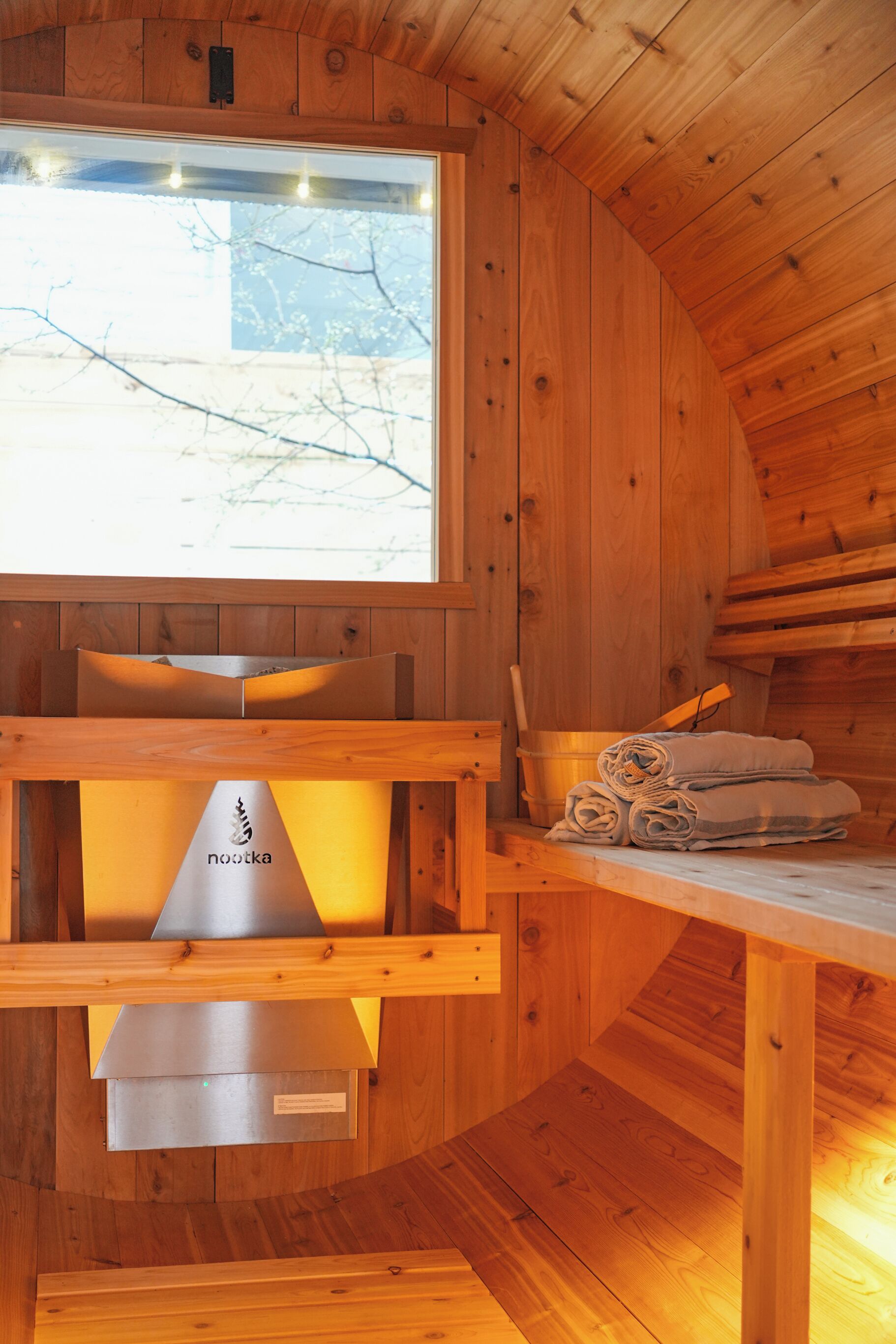 A wooden cabin interior with a sauna, a wooden table, and a window with a view of trees.