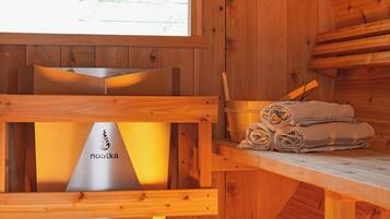 A wooden cabin interior with a sauna, a wooden table, and a window with a view of trees.