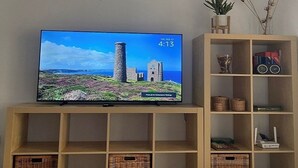 A television on a wooden stand displaying a castle and date/time. - Modern, Stylish Beach Apartment with Stunning sea views, Pools & Ultrafast Wi-Fi (La'Azohia)