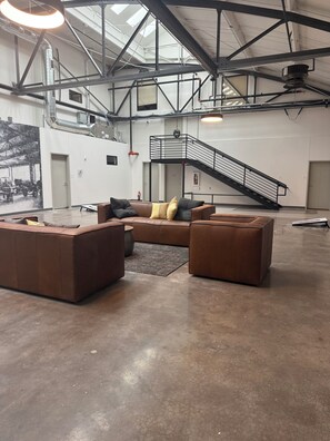 Amplia habitación de estilo industrial con techo alto, vigas a la vista y una escalera.