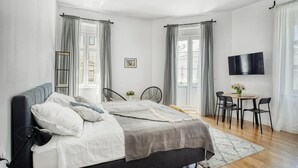 A modern bedroom with a bed, bedside tables, a TV, and a dining area with chairs and a table. - Berry Berry studios by Flat White (Zagreb)