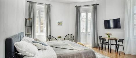 A modern bedroom with a bed, bedside tables, a TV, and a dining area with chairs and a table.