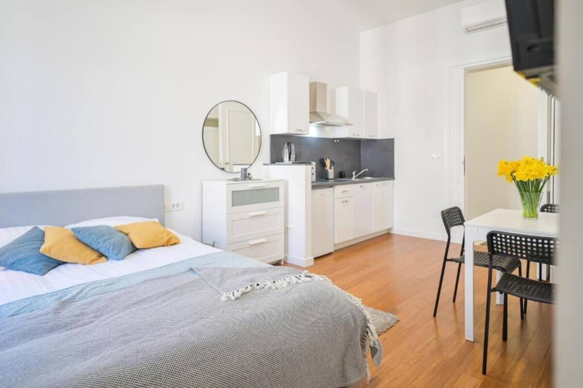 Ein modernes Schlafzimmer mit Bett, Nachttisch und einer kleinen Küchenzeile.