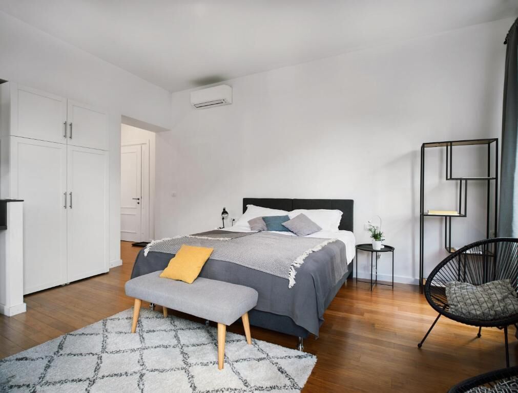 Un dormitorio moderno con una cama, un banco, una silla y una mesita de noche.