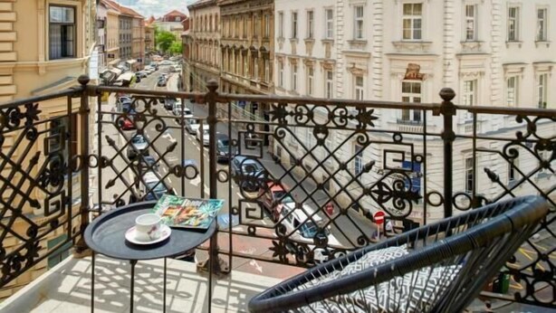 A balcony with a chair and table, overlooking a street with historic buildings and parked cars. - Berry Berry studios by Flat White (Zagreb)