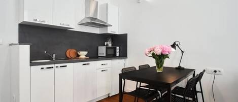 Une cuisine moderne avec des armoires blanches, un comptoir noir et une hotte de cuisinière en acier inoxydable. On y trouve une table à manger avec quatre chaises et un vase de fleurs.