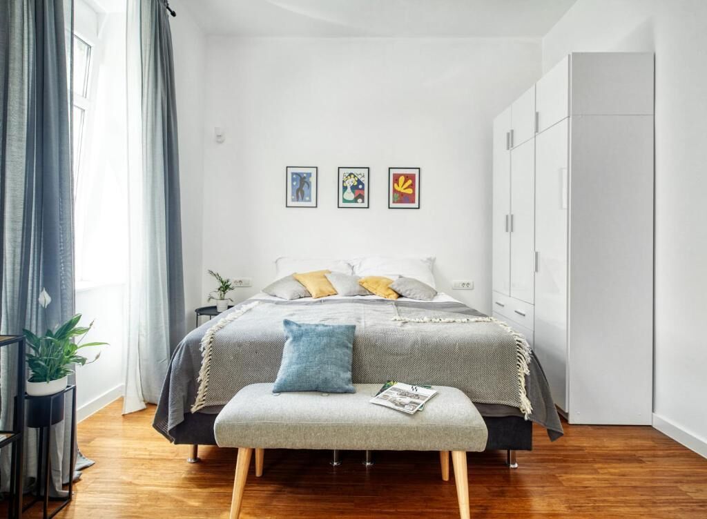 A bedroom with a bed, a bench, a wardrobe, and three framed pictures on the wall.