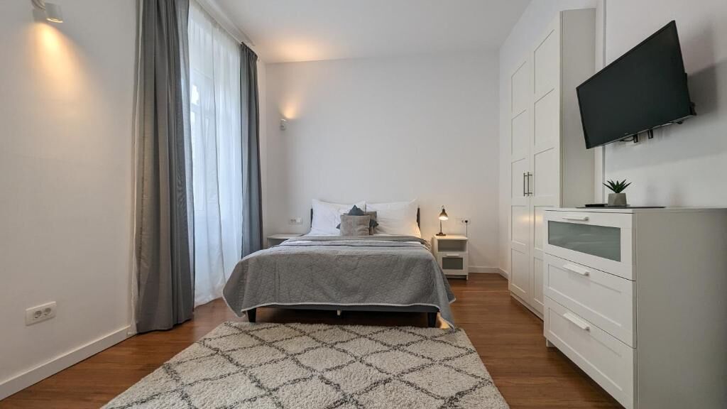 Ein modernes Schlafzimmer mit Bett, Nachttischen, Fernseher und Kleiderschrank.