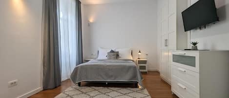Un dormitori modern amb un llit, taules de nit, televisió i un armari.