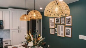 A modern kitchen with white cabinets, a dining table set with plates and cutlery, and a vase of flowers. There are two hanging wicker lamps and framed pictures on the wall. - Charming Detached Bungalow in Historic Old Town Monrovia Kingsize Bed！ (Monrovia)