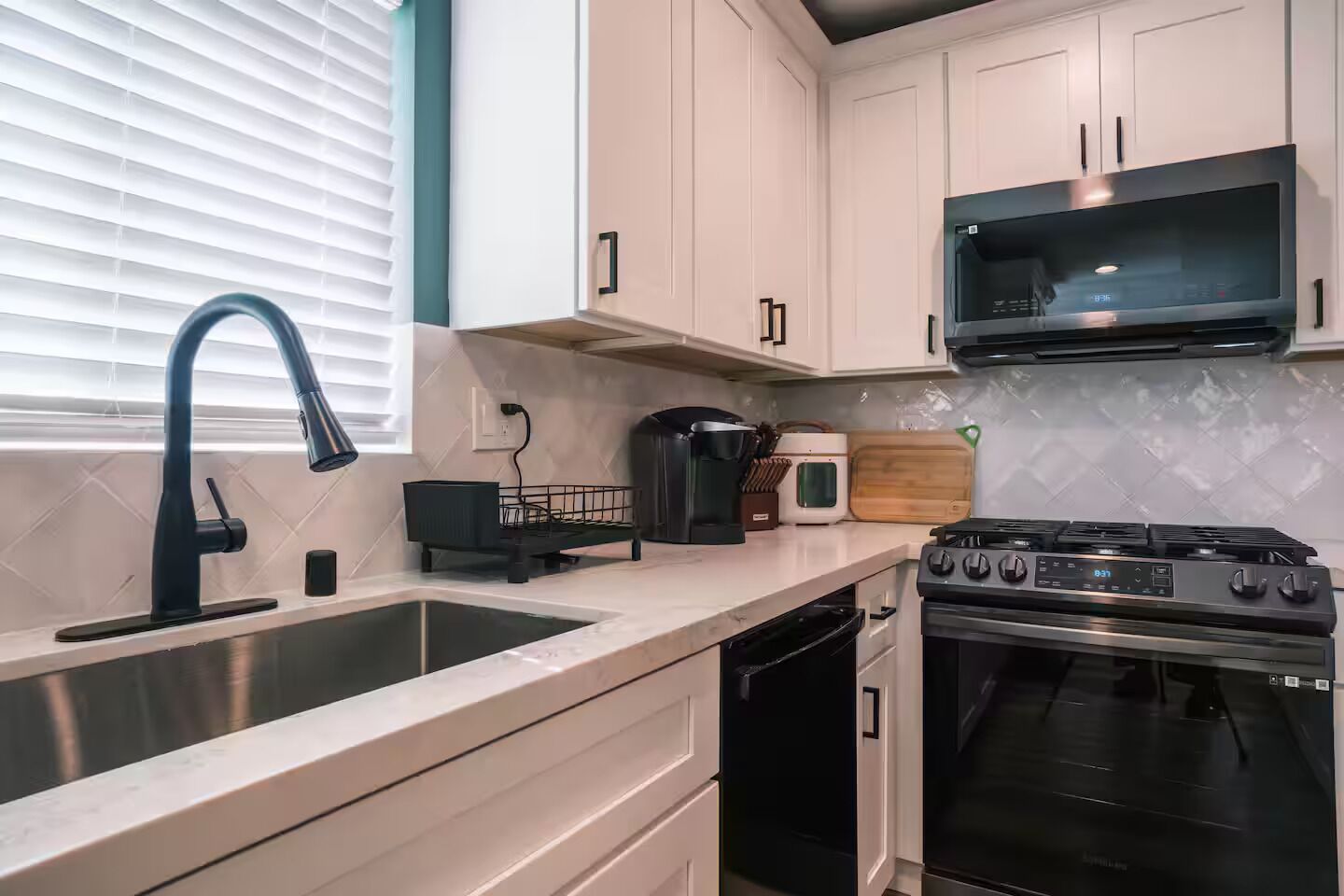A modern kitchen with a stainless steel sink, a black faucet, a microwave, a stove, and a toaster.