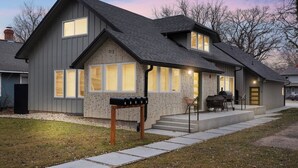Ein modernes, zweistöckiges Haus mit grauer Fassade, großen Fenstern und einer überdachten Veranda mit Sitzgelegenheiten.