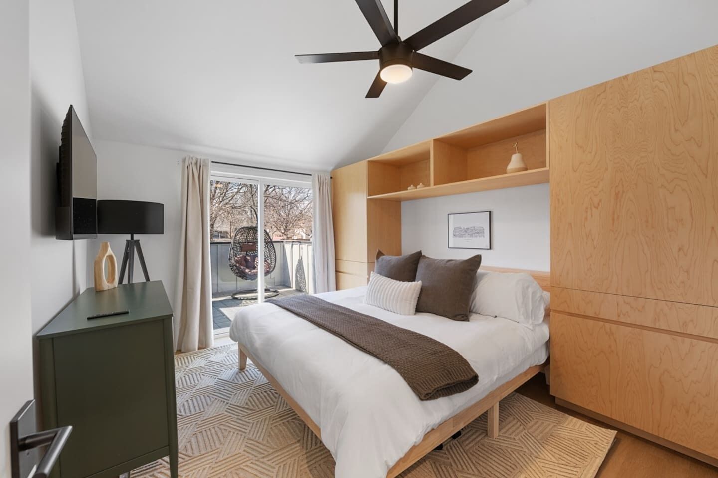 Une chambre à coucher comprenant un lit, un ventilateur de plafond, une télévision et une porte-fenêtre coulissante donnant sur un balcon.