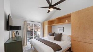Ein Schlafzimmer mit Bett, Deckenventilator, Fernseher und einer Schiebetür zu einem Balkon.
