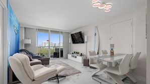 Un salón moderno con una mesa de vidrio, sillas blancas, un sofá, un televisor y vistas a la ciudad.