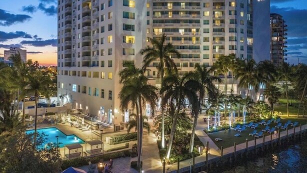 Un hotel de varios pisos con piscina, palmeras y vista al agua.
