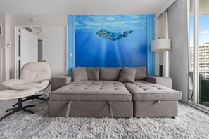 Ein modernes Schlafzimmer mit Ecksofa, einem Sessel, einem großen Fenster und einer Wandmalerei.